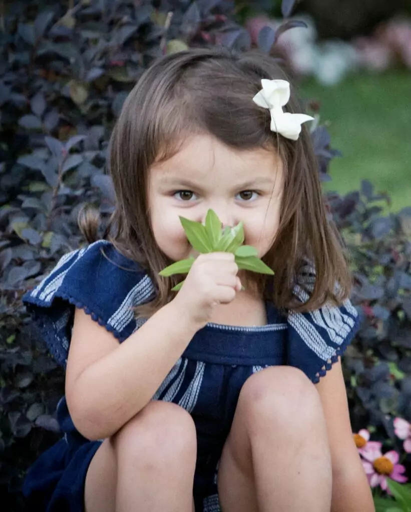 Little girl smelling a flower sitting in the garden.